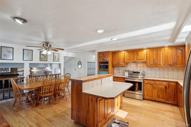 kitchen with stainless steel electric range oven, light wood finished floors, light countertops, wall oven, and a kitchen island