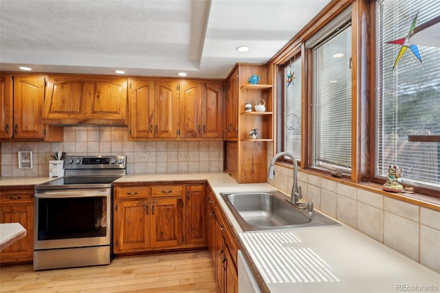 kitchen with brown cabinets, light countertops, a sink, stainless steel electric range, and exhaust hood