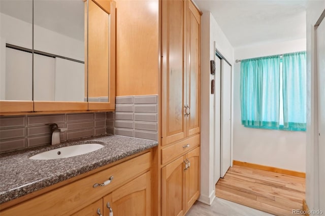 bathroom with vanity, baseboards, backsplash, and wood finished floors