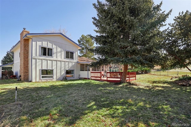 rear view of house with a yard, a chimney, board and batten siding, fence, and a wooden deck