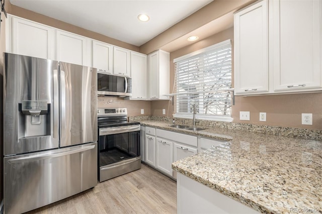 kitchen with appliances with stainless steel finishes, white cabinetry, sink, light stone counters, and light hardwood / wood-style flooring