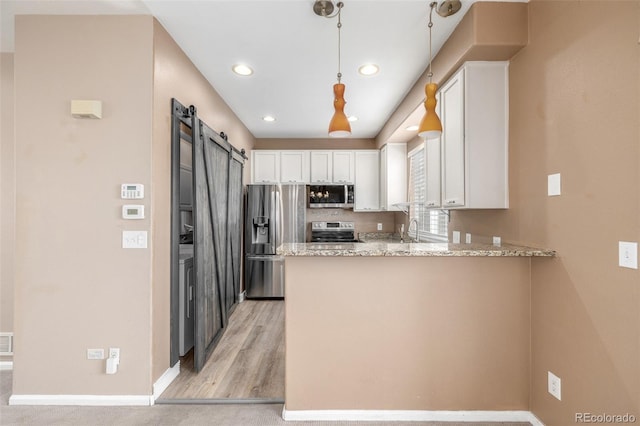 kitchen featuring white cabinetry, stainless steel appliances, a barn door, and kitchen peninsula