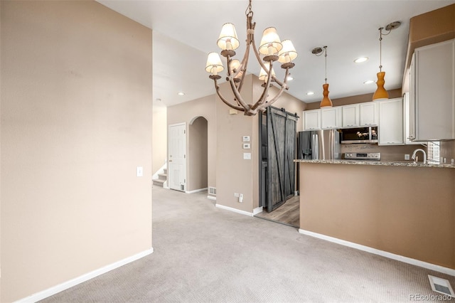 kitchen with pendant lighting, light colored carpet, stainless steel appliances, a barn door, and white cabinets