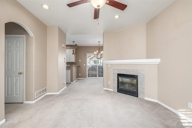 unfurnished living room with a tiled fireplace, ceiling fan with notable chandelier, and light carpet