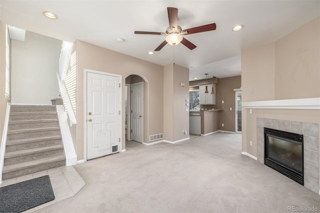 unfurnished living room with a tiled fireplace, light carpet, and ceiling fan