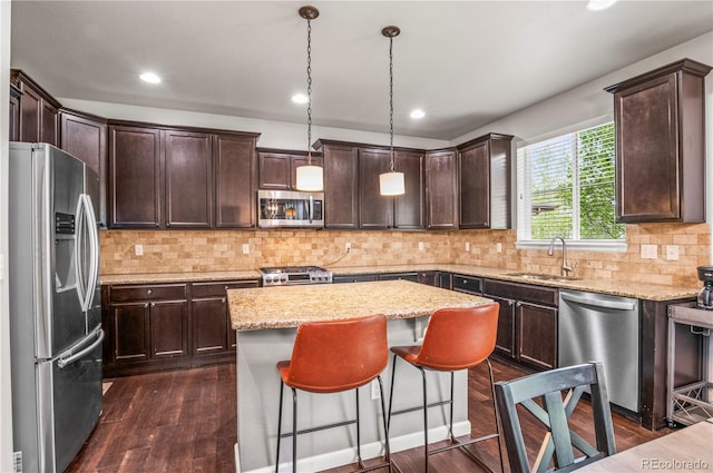 kitchen with dark brown cabinetry, a sink, a center island, stainless steel appliances, and dark wood-type flooring