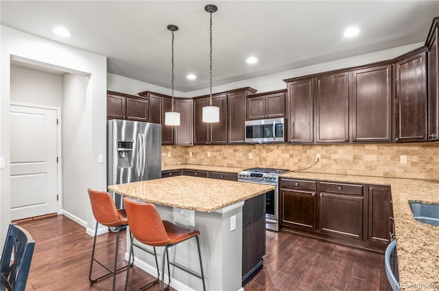 kitchen featuring dark wood-style flooring, dark brown cabinets, appliances with stainless steel finishes, a breakfast bar area, and a kitchen island