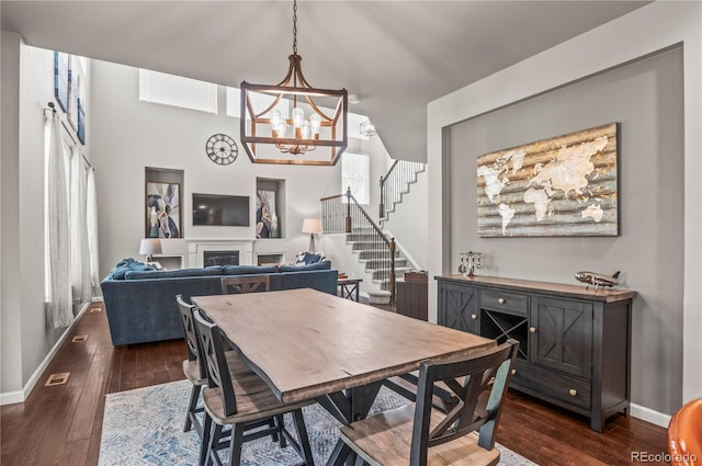 dining room featuring an inviting chandelier, baseboards, a fireplace, and dark wood-style floors