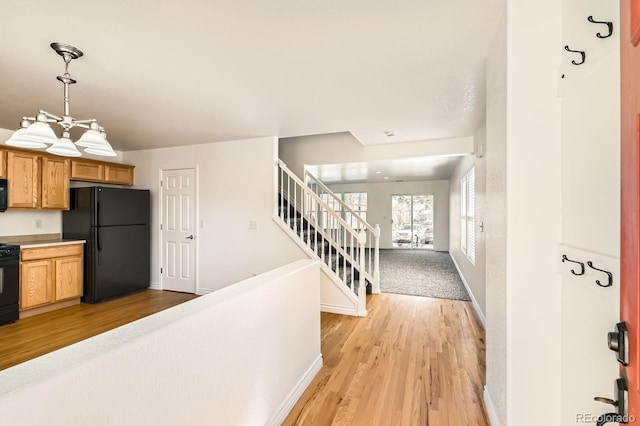 kitchen featuring baseboards, light wood-style floors, black appliances, and hanging light fixtures