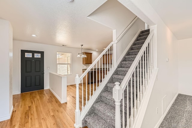 entrance foyer featuring light wood finished floors, a textured ceiling, stairs, and baseboards