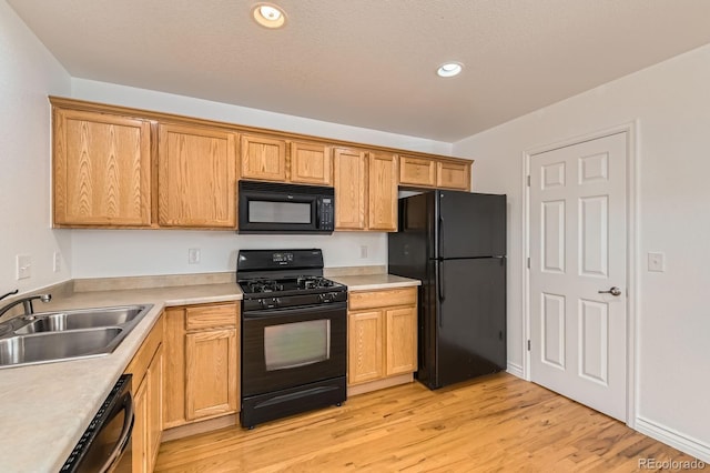 kitchen with black appliances, light wood-style flooring, a sink, recessed lighting, and light countertops