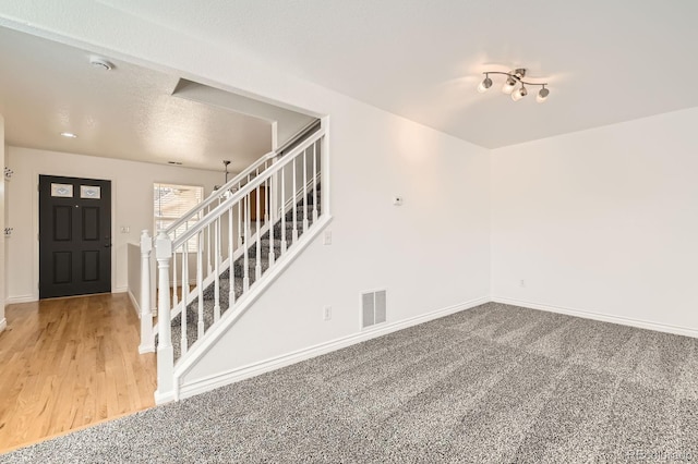 carpeted foyer with stairs, baseboards, visible vents, and a textured ceiling