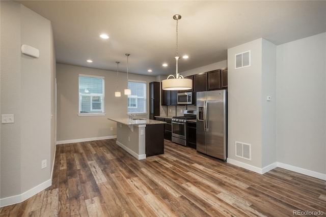 kitchen featuring a breakfast bar, light stone counters, decorative light fixtures, stainless steel appliances, and a kitchen island with sink