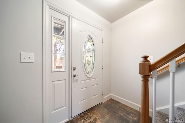 foyer entrance featuring stone finish flooring, baseboards, and stairs