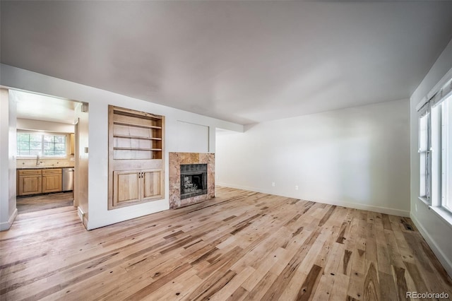 unfurnished living room with light wood-style floors, a sink, a tile fireplace, and baseboards