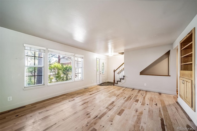 unfurnished living room with light wood-style floors, stairs, and baseboards
