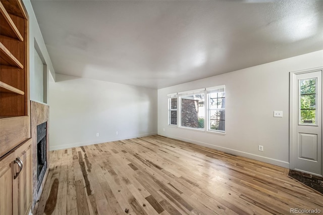 unfurnished living room with light wood-style flooring, a fireplace, and baseboards