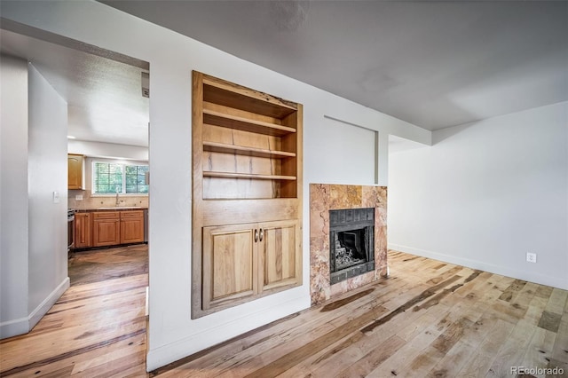 unfurnished living room featuring light wood-type flooring, a tile fireplace, built in shelves, a sink, and baseboards