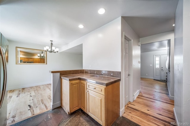 kitchen featuring a chandelier, dark countertops, wood finished floors, baseboards, and light brown cabinetry
