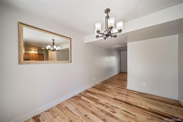 unfurnished dining area featuring a chandelier, wood-type flooring, and baseboards