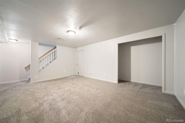 unfurnished living room with carpet flooring, stairway, baseboards, and a textured ceiling