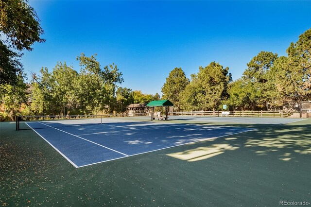 view of tennis court featuring fence and view of scattered trees