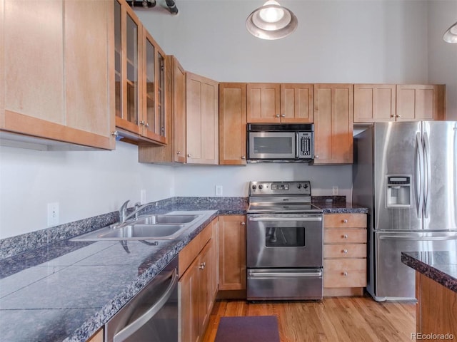 kitchen with stainless steel appliances, dark countertops, light wood-style flooring, glass insert cabinets, and a sink