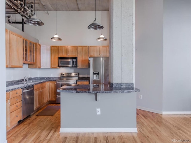 kitchen with dark stone counters, stainless steel appliances, a high ceiling, and light wood-style flooring