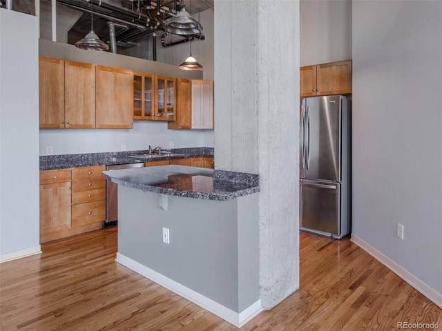 kitchen featuring light wood finished floors, baseboards, glass insert cabinets, stainless steel appliances, and a sink