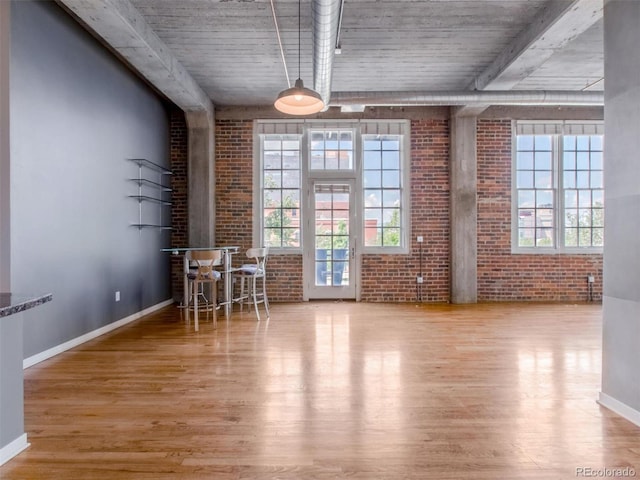 unfurnished dining area with brick wall, wood finished floors, and baseboards