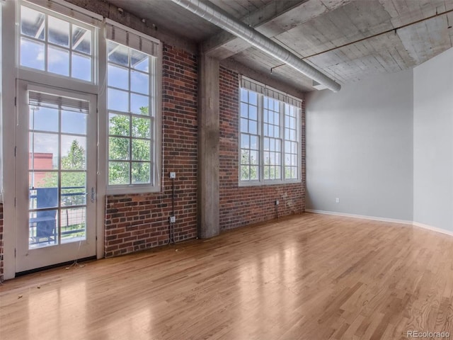 unfurnished room featuring brick wall, wood finished floors, and baseboards