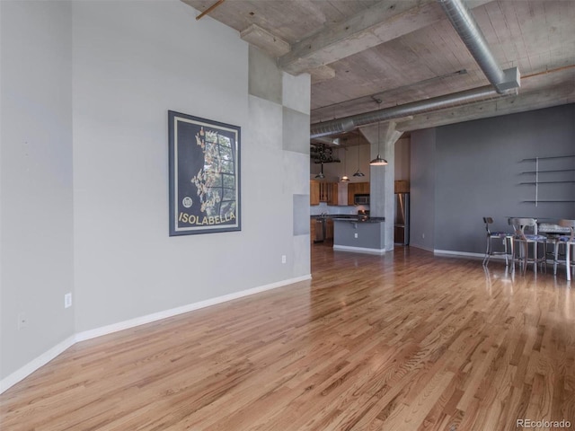 unfurnished living room featuring baseboards, a towering ceiling, and light wood-style floors