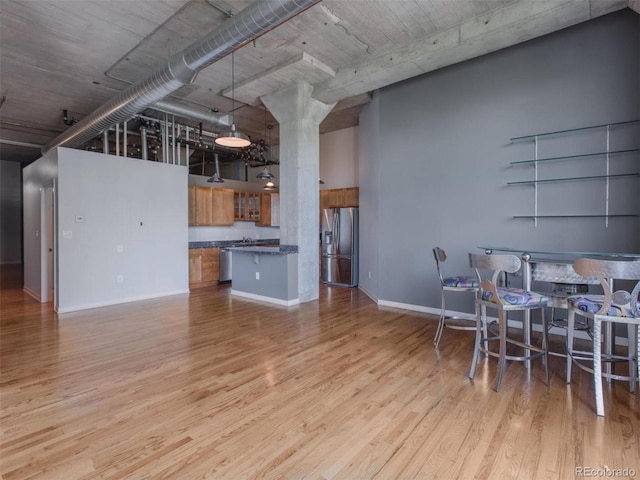 kitchen featuring a high ceiling, wood finished floors, appliances with stainless steel finishes, brown cabinets, and dark countertops