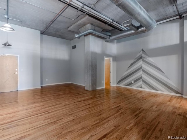 empty room with baseboards, a high ceiling, visible vents, and wood finished floors