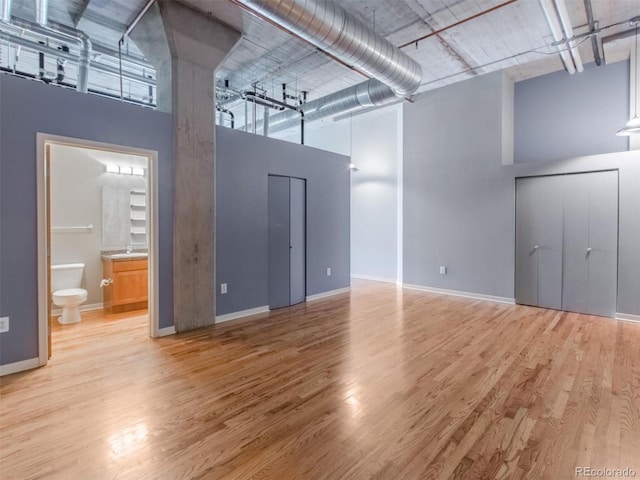 interior space featuring baseboards, ensuite bath, wood finished floors, a high ceiling, and a sink