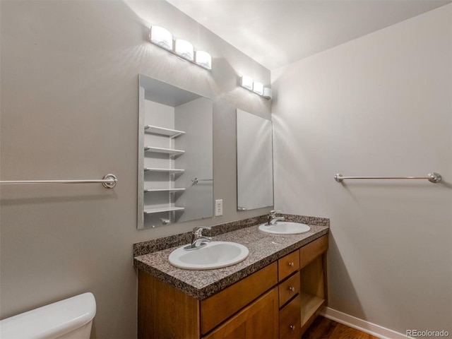 bathroom featuring baseboards, a sink, toilet, and double vanity