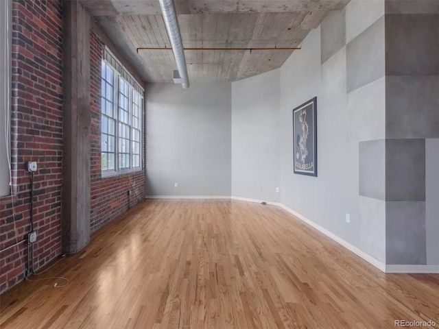 empty room with baseboards, brick wall, and wood finished floors