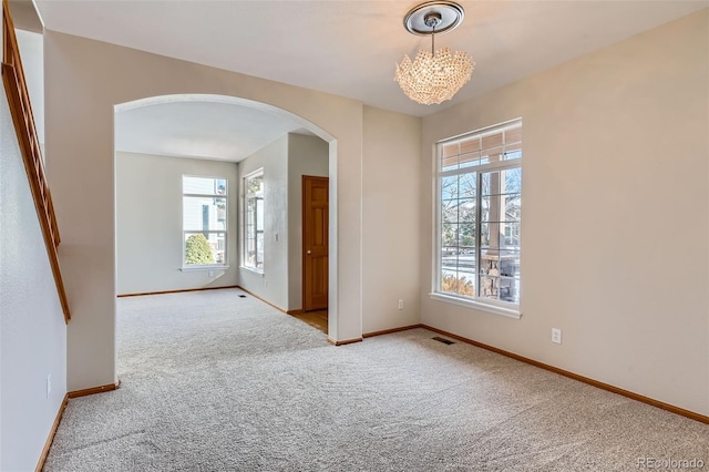 carpeted spare room with plenty of natural light and a notable chandelier