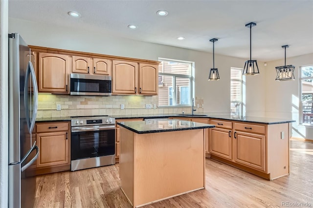 kitchen with pendant lighting, stainless steel appliances, a kitchen island, and a wealth of natural light