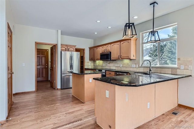 kitchen with kitchen peninsula, appliances with stainless steel finishes, dark stone counters, light hardwood / wood-style floors, and a kitchen island