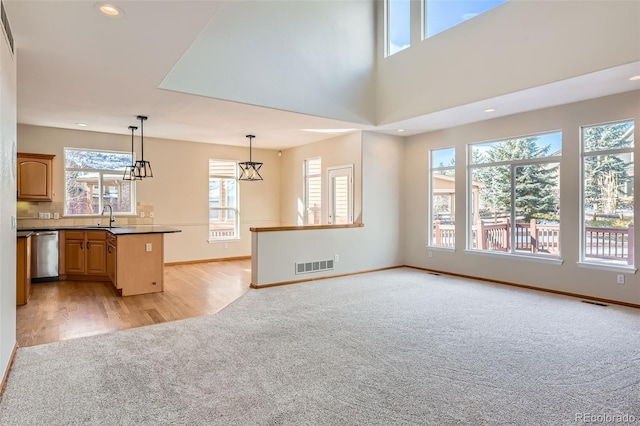 kitchen featuring pendant lighting, sink, stainless steel dishwasher, light wood-type flooring, and a towering ceiling