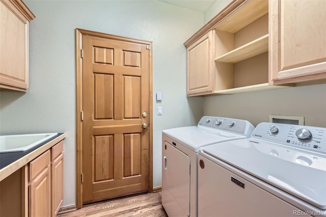 clothes washing area with washer and dryer, cabinets, and light hardwood / wood-style flooring