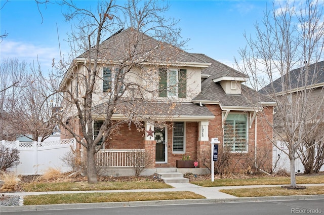 view of front of house with roof with shingles, fence, a porch, and brick siding