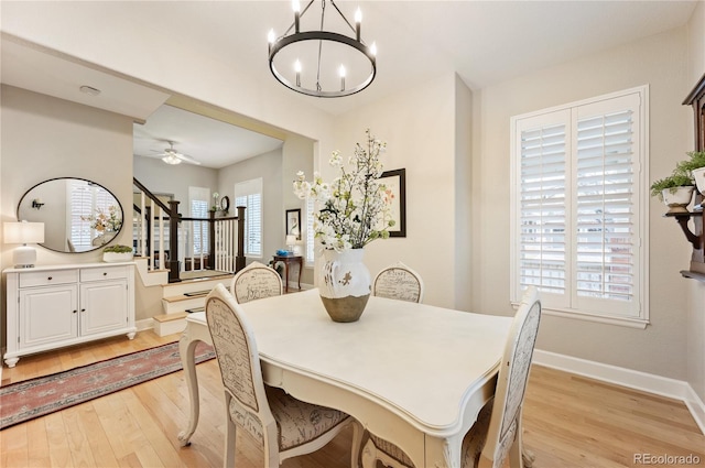 dining space featuring light wood finished floors, baseboards, stairway, and ceiling fan with notable chandelier