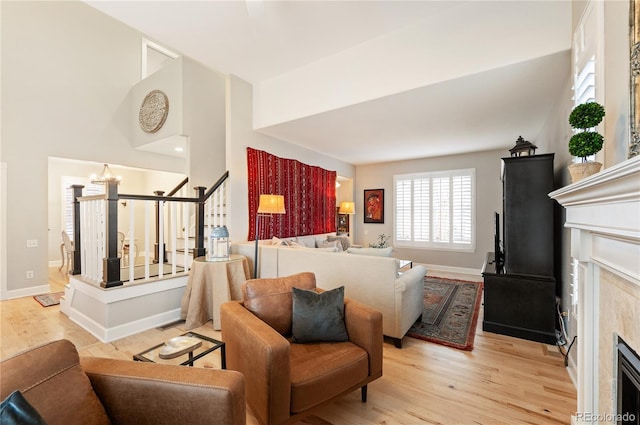 living area with baseboards, an inviting chandelier, stairs, light wood-style floors, and a fireplace