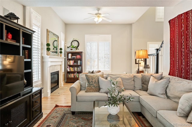 living area with light wood-type flooring, stairs, a fireplace, and a ceiling fan