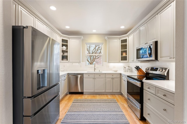 kitchen featuring stainless steel appliances, a sink, light countertops, light wood-type flooring, and glass insert cabinets