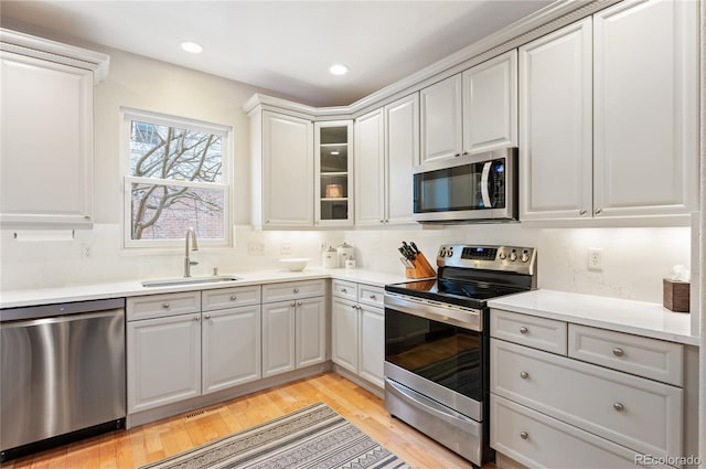 kitchen featuring light wood-style flooring, a sink, light countertops, appliances with stainless steel finishes, and glass insert cabinets