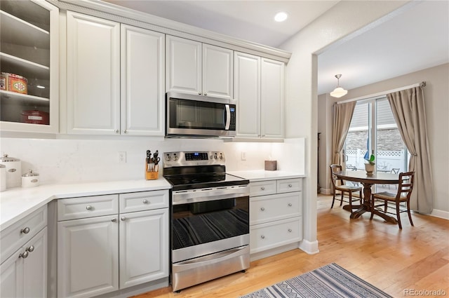 kitchen with stainless steel appliances, white cabinets, light wood-style floors, light countertops, and glass insert cabinets