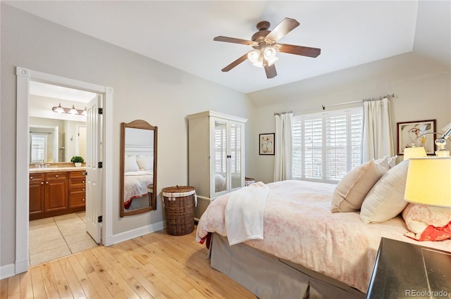 bedroom featuring lofted ceiling, ceiling fan, connected bathroom, light wood-style flooring, and baseboards